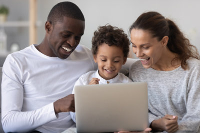 Happy family mom dad and little kid son enjoy using laptop watching cartoons